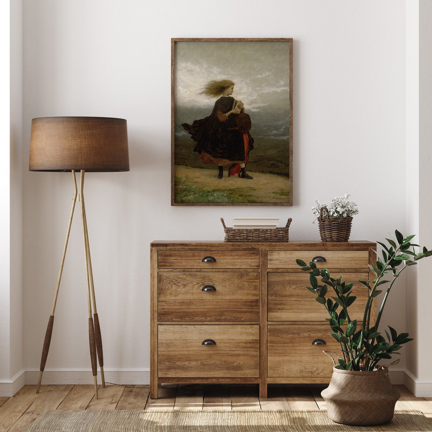 Wooden dresser with a lamp, plant, and portrait print, in a room.