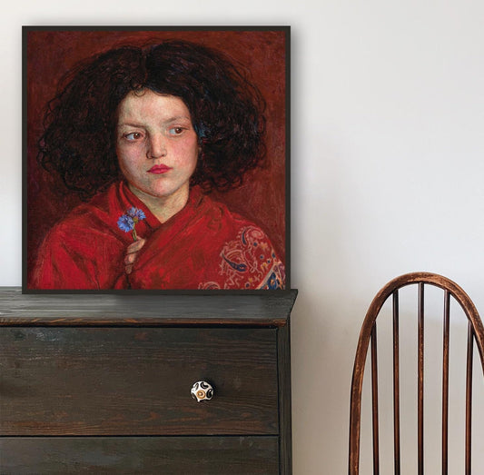 A fine art print of a beautiful oil painting of a young girl in a red shawl. The print is displayed in a thin black picture frame on top of a dark chest of drawers.