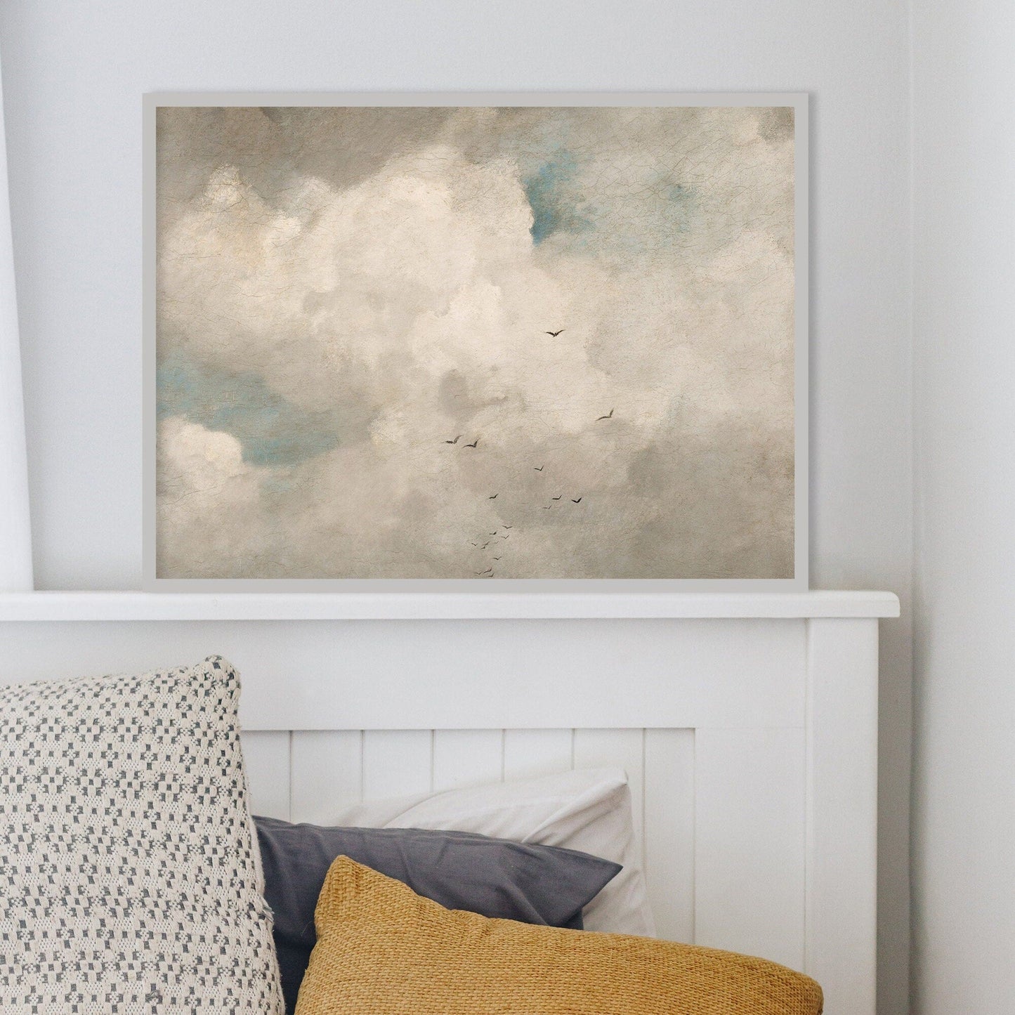 Bed with colorful pillows and a framed artwork of clouds on the wall.