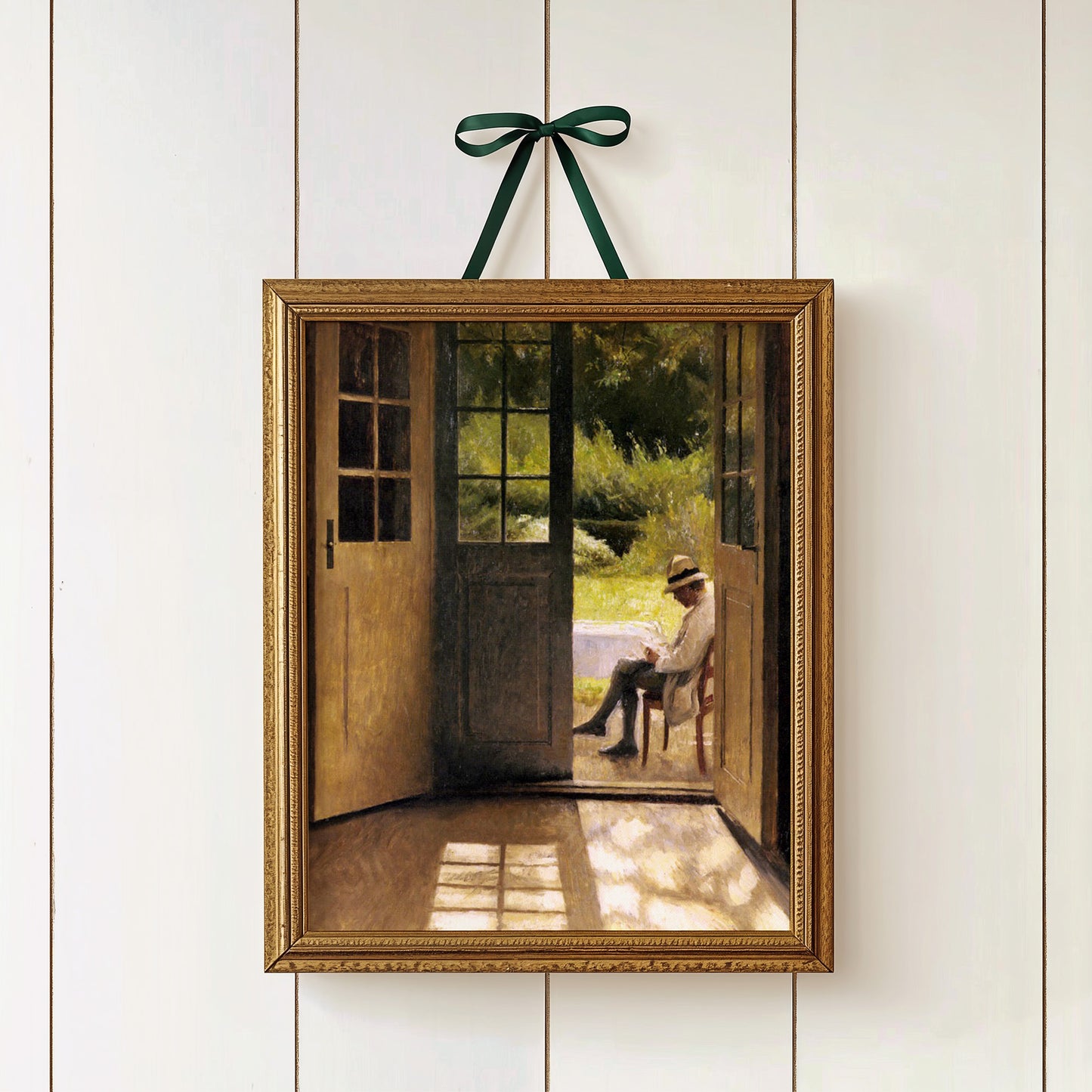 Framed artwork of a man sitting on a chair in a garden, hanging on a white wall.