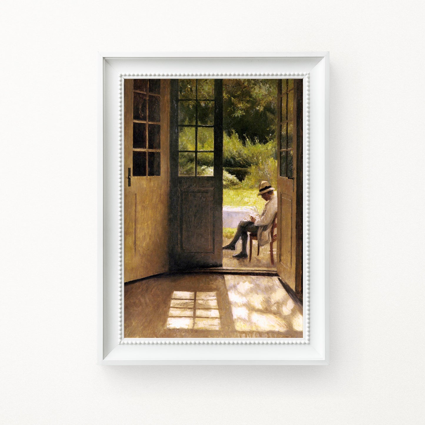Framed artwork of a man sitting on a chair by a door, reading a book in a white frame hung on a white wall