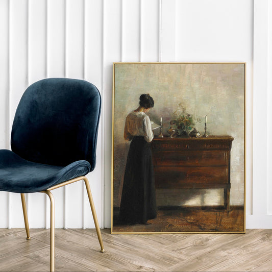 Framed painting of a woman by a desk, next to a dark blue velvet chair with gold legs, on a wooden floor.
