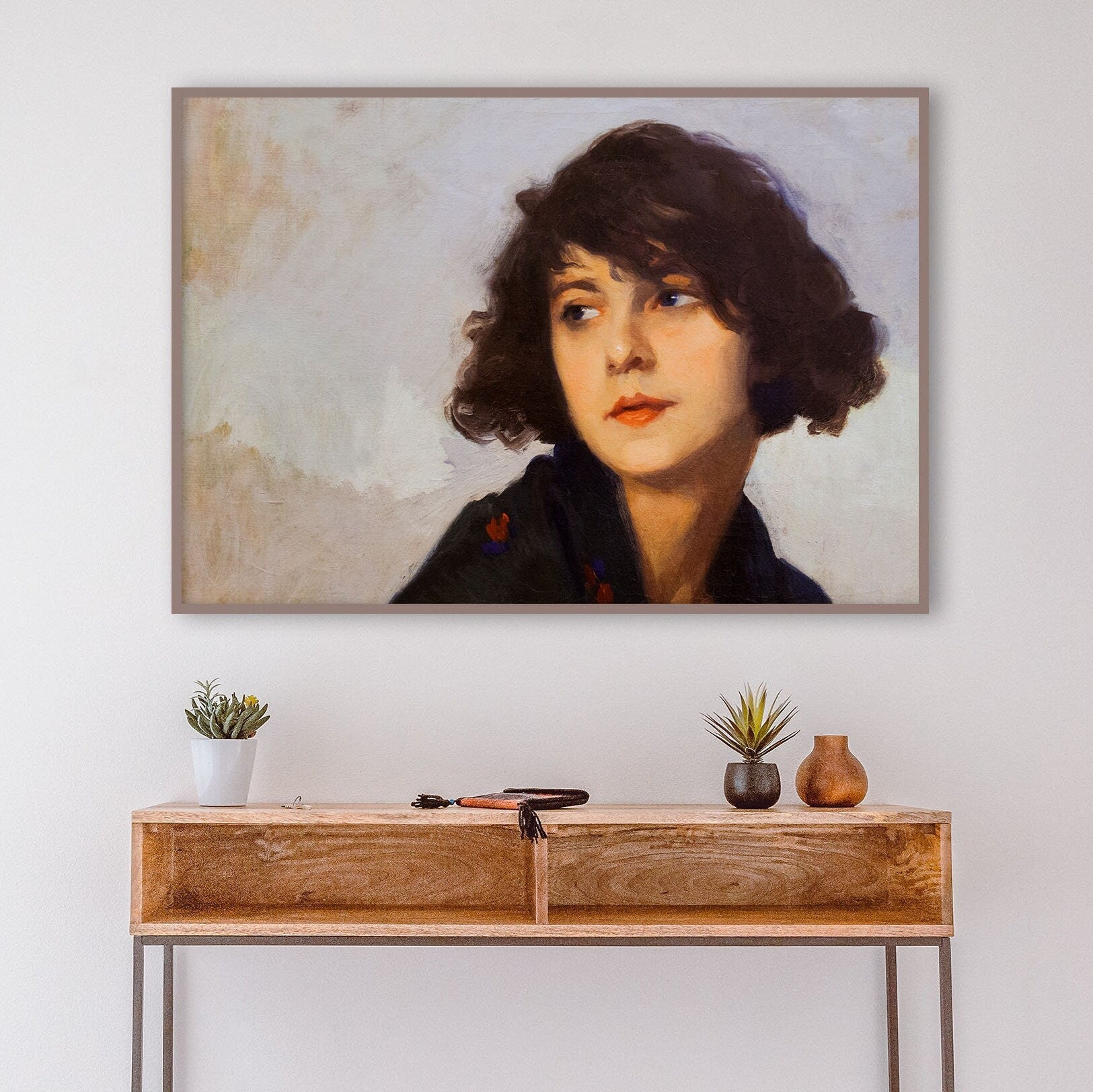 A fine art print of a portrait in oil of a young lady from the Art Deco period. The print is displayed in a thin wood picture frame over a console table.