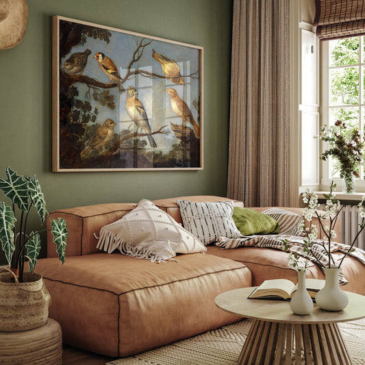 A framed print of garden birds gathered together on the branches of a tree. The print is displayed hanging on the wall in a luxury living room above a brown leather sofa.