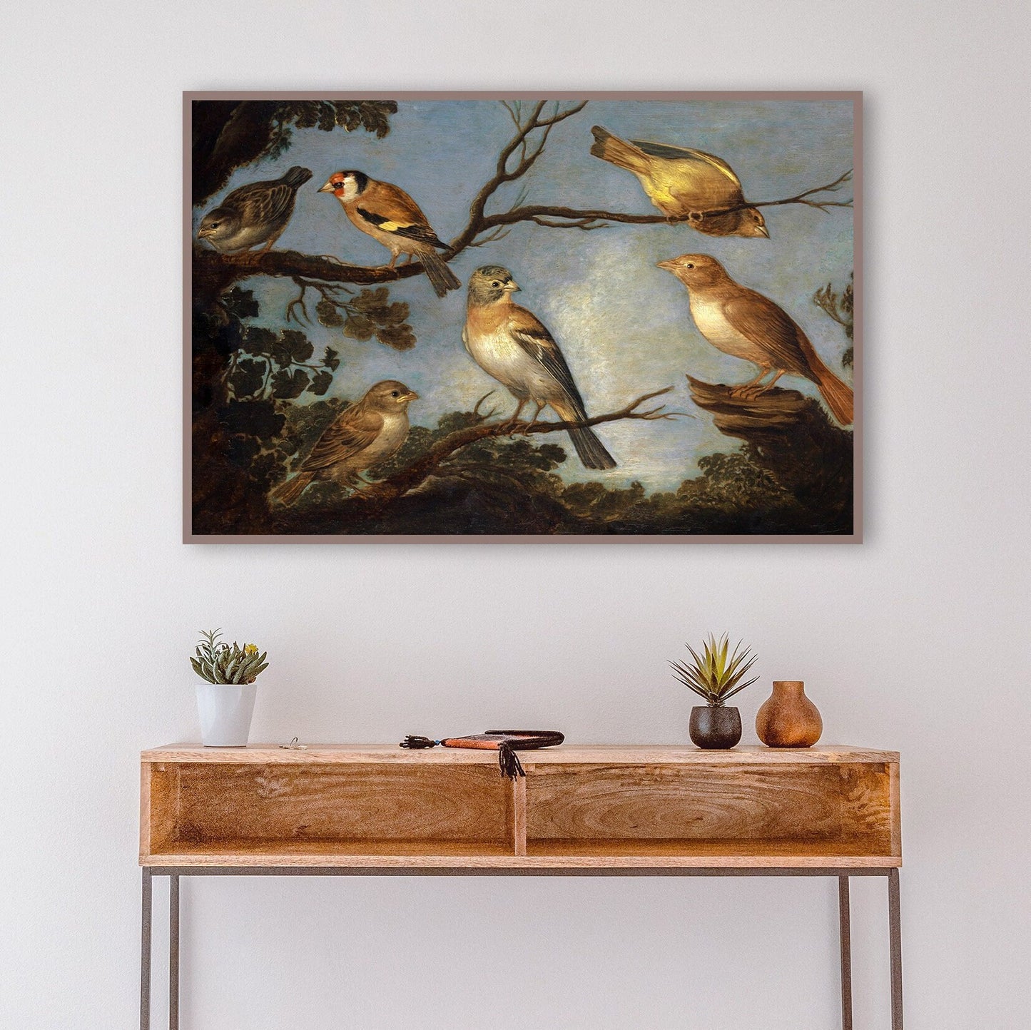 A framed print of garden birds gathered together on the branches of a tree. The print is displayed hanging on the wall in above a wooden console table in an entryway.