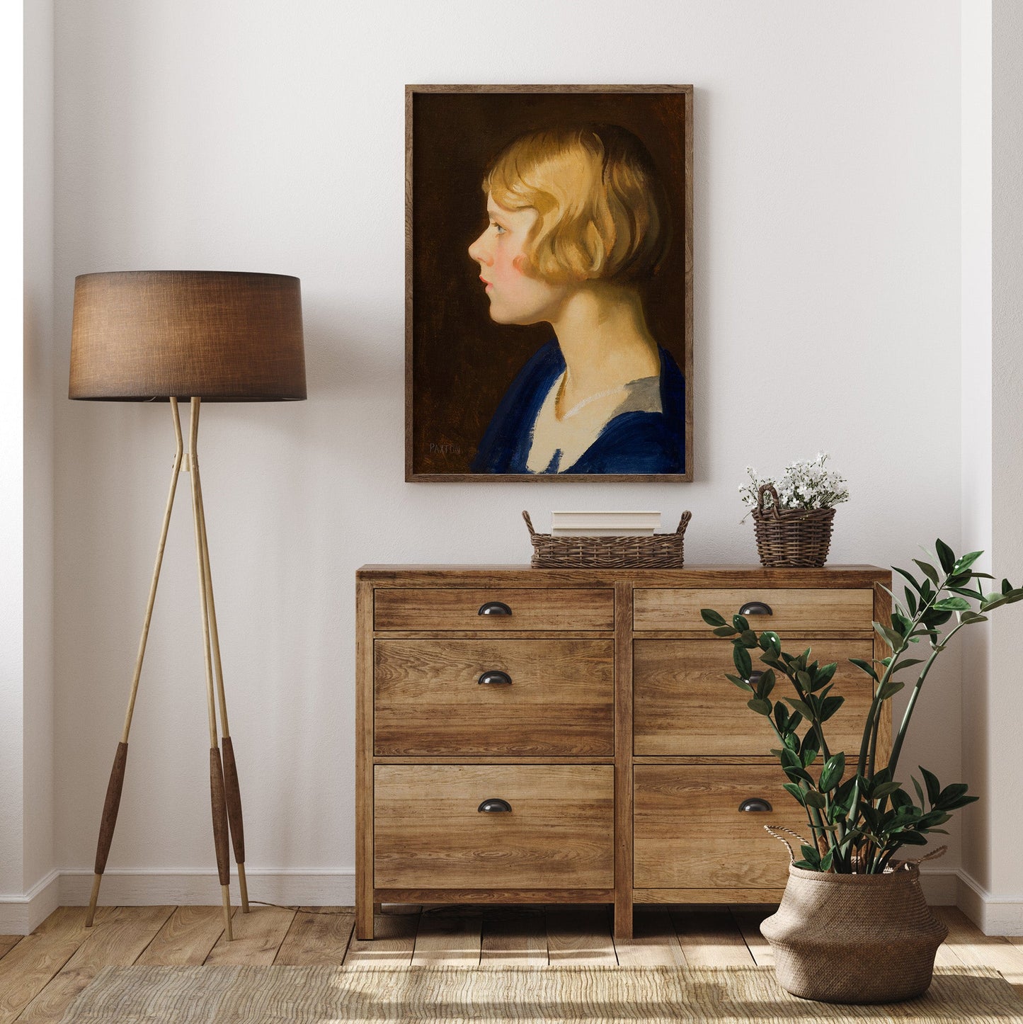 Wooden dresser with a lamp, plant, and portrait on a white wall.