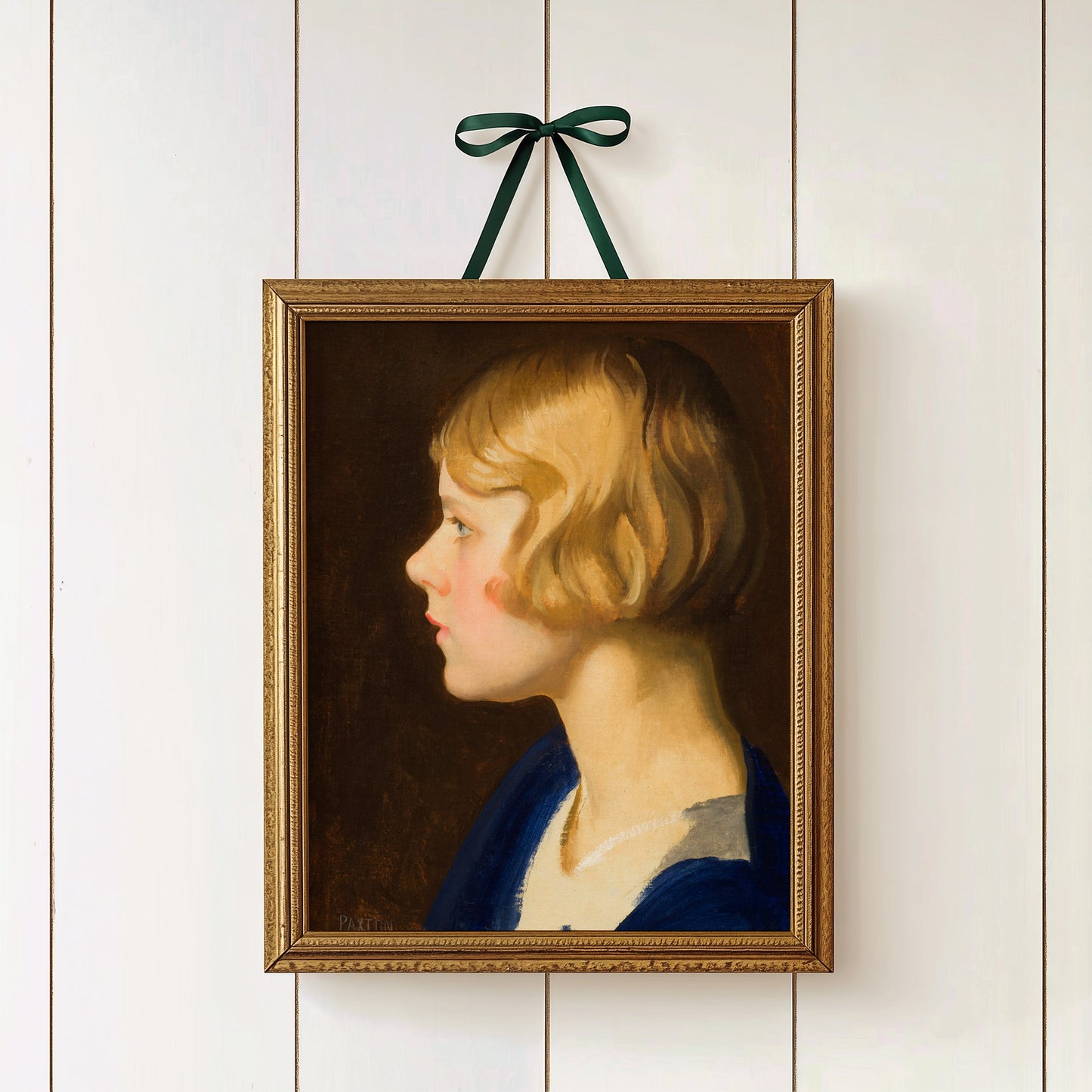 Framed portrait of a young girl with blonde hair and a blue dress, hanging on a white wall.