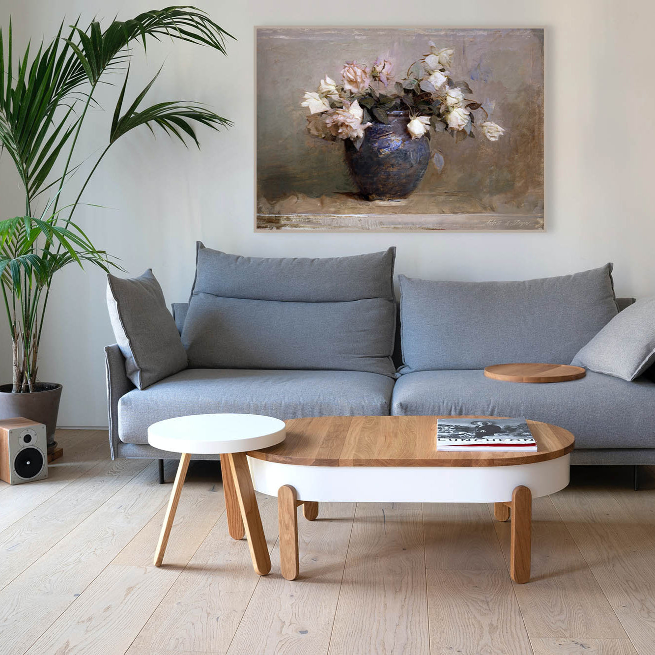 Modern living room with framed fine art print of roses in a vase above a gray sofa, wooden coffee table, and decorative plants.