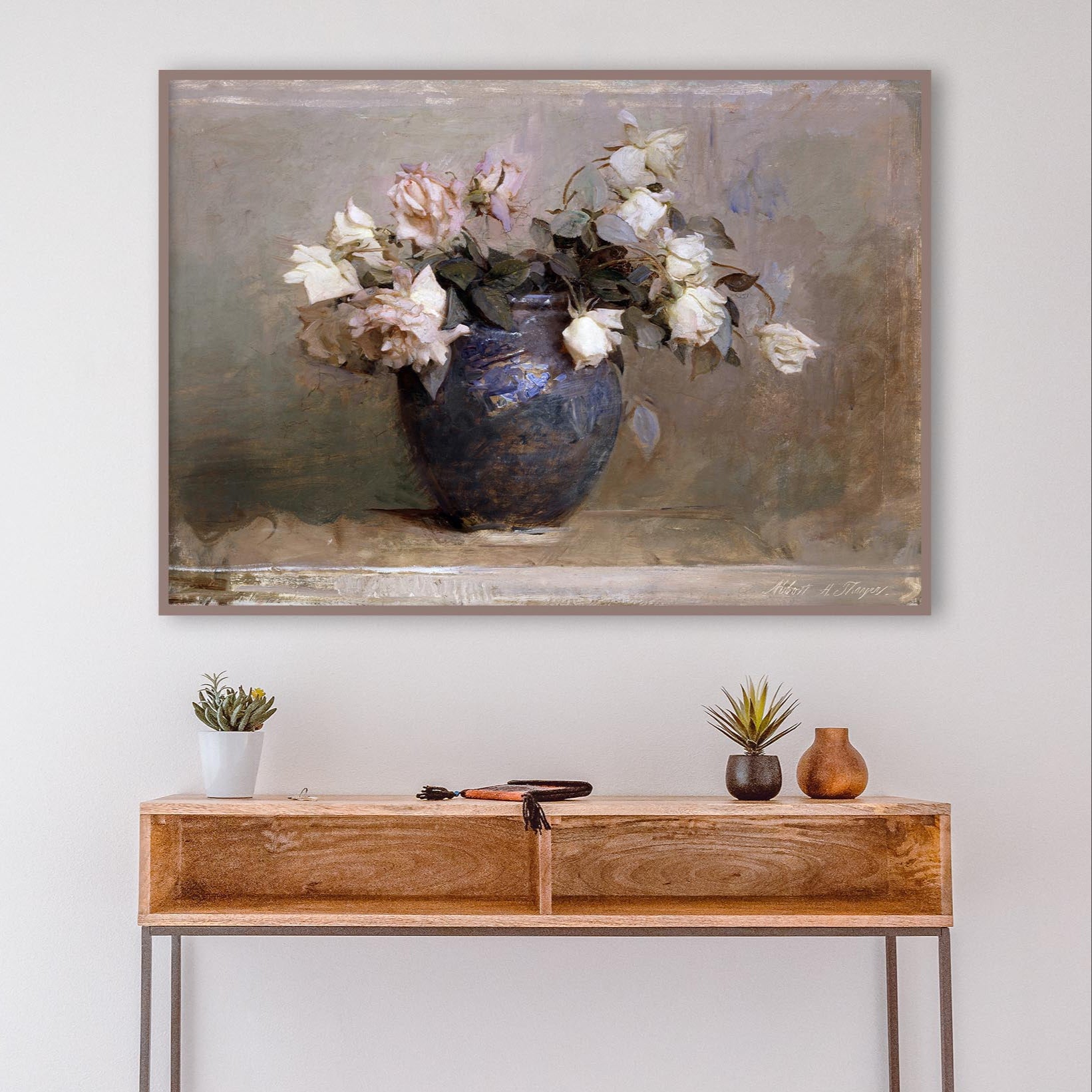 Wooden console table with decorative items against a white wall with a framed floral print of roses in a blue vase.