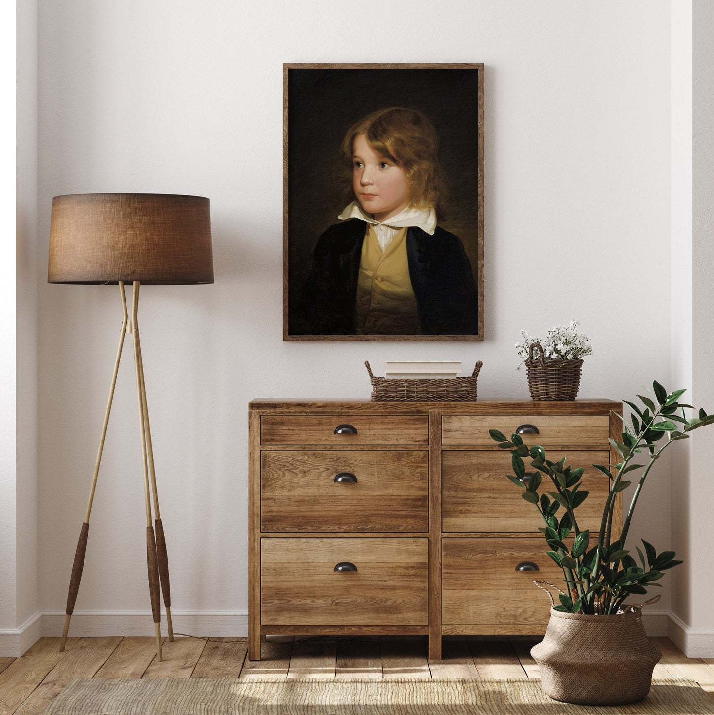 Wooden dresser with a lamp, plant, and portrait on a white wall.