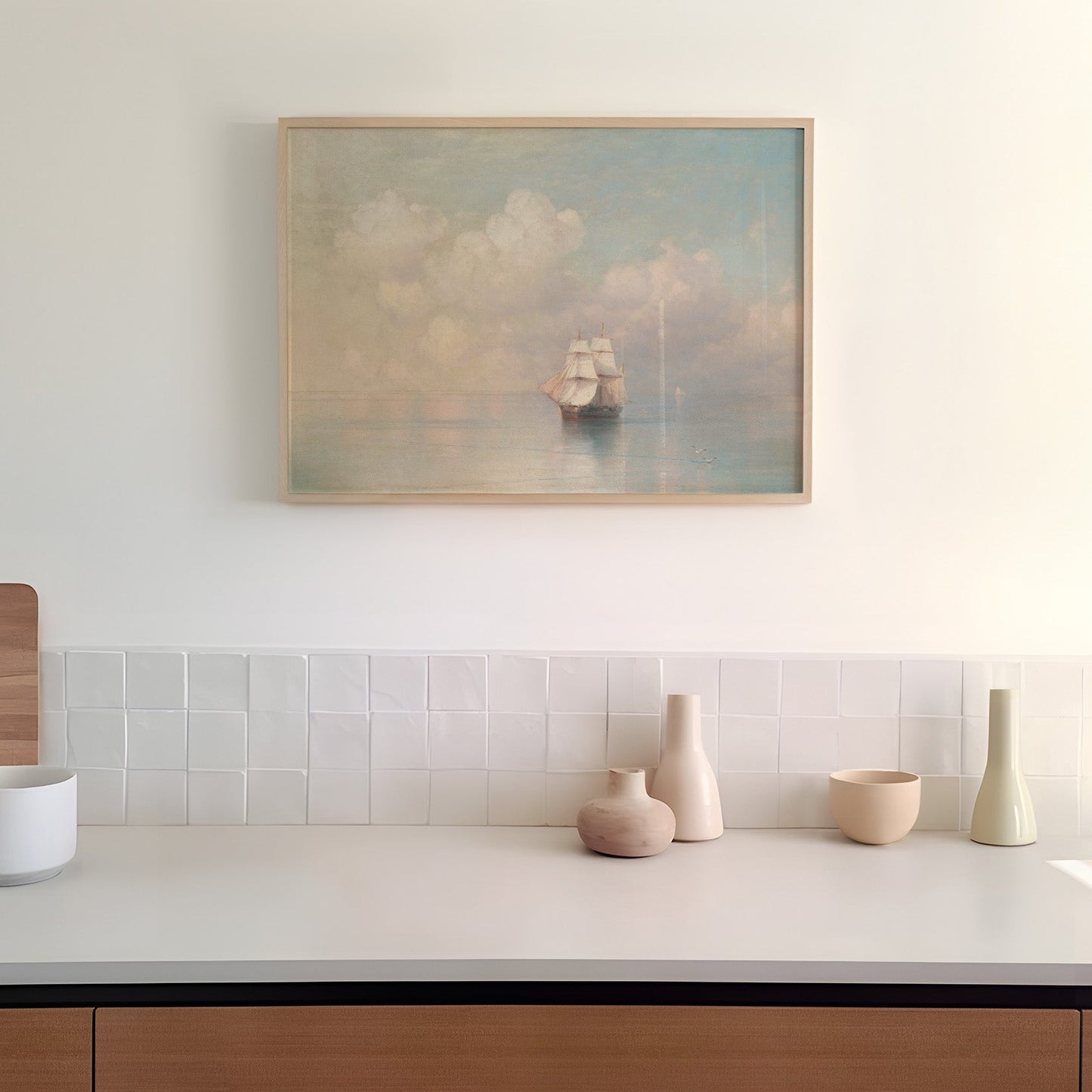 Framed artwork of a ship on a cloudy sky above a kitchen counter with decorative vases.