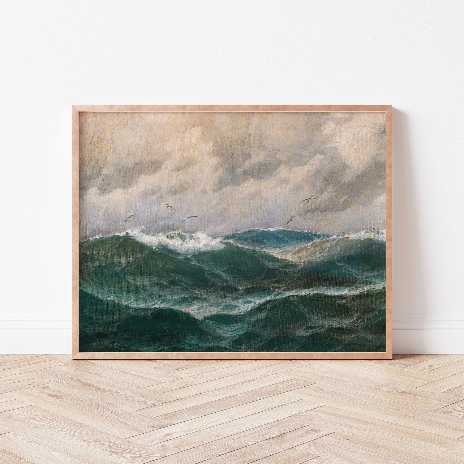 Framed artwork of a seascape with turbulent waves and cloudy sky leaning against a white wall.