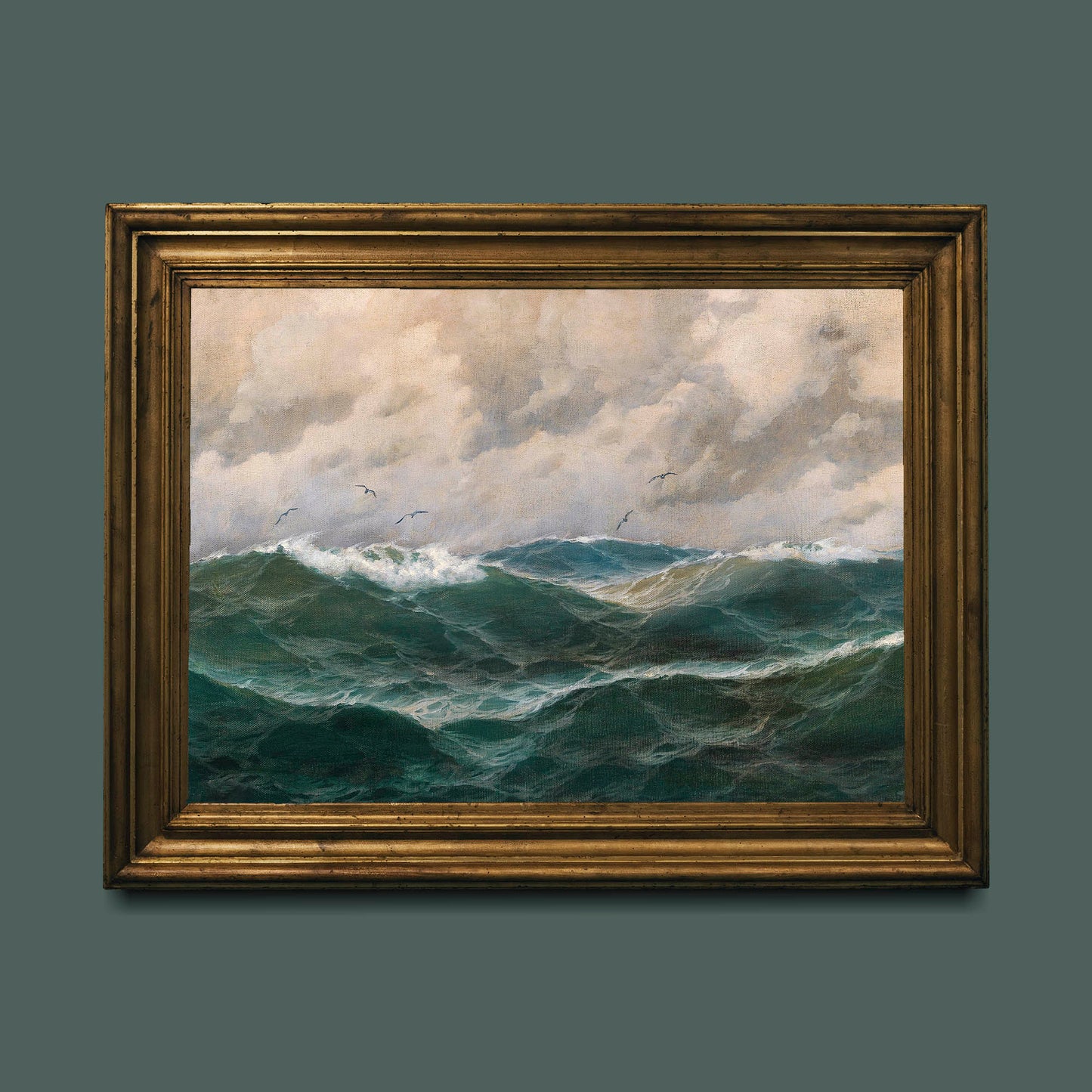 Framed fine art print of a stormy sea with waves and clouds. The print is displayed hanging on a teal coloured wall in a gold picture frame.