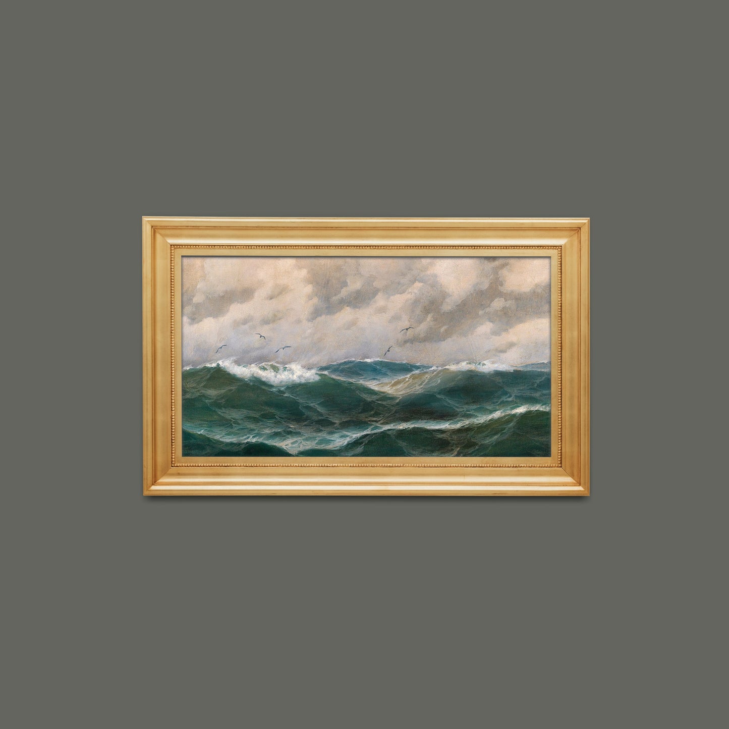 Framed fine art print of a stormy sea and dramatic clouds, hung on a grey wall in a gold picture frame.