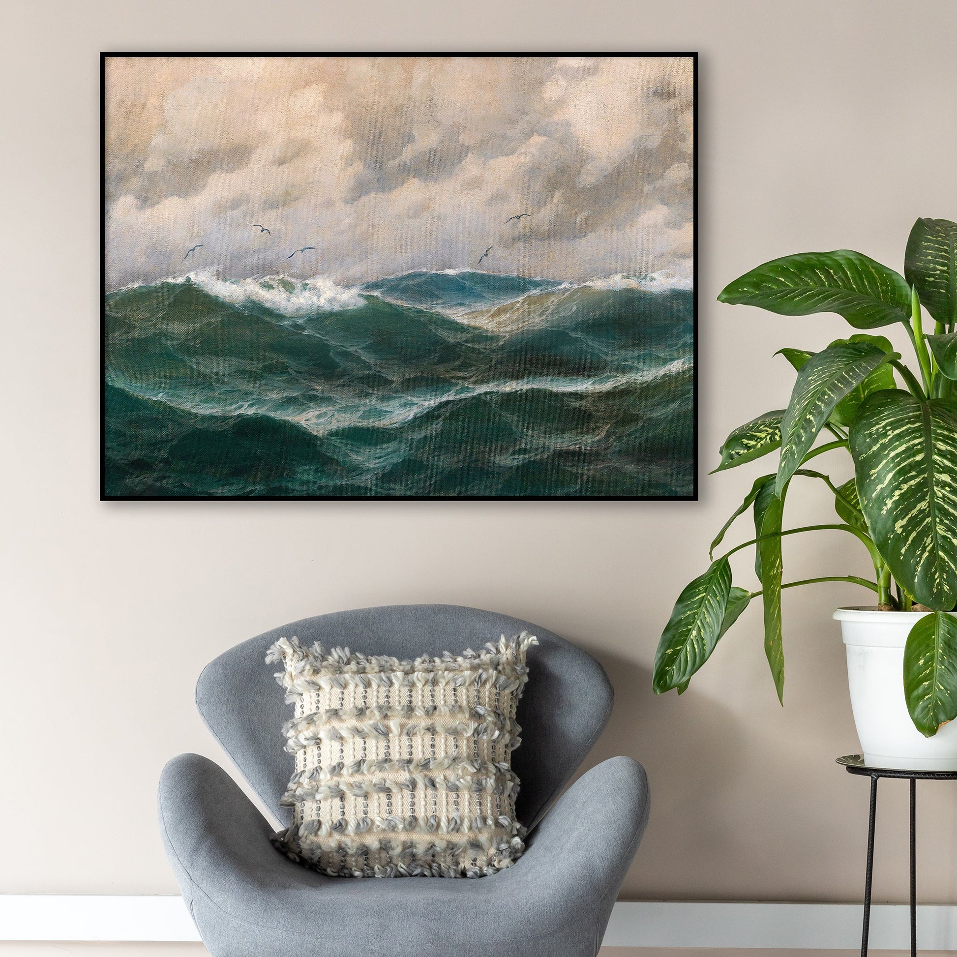Gray armchair with a textured pillow in a room with a large fine art print of a stormy sea and sky, hung on the wall in a thin black picture frame.