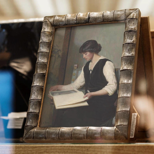 Framed print of a woman holding a book in a decorative frame.