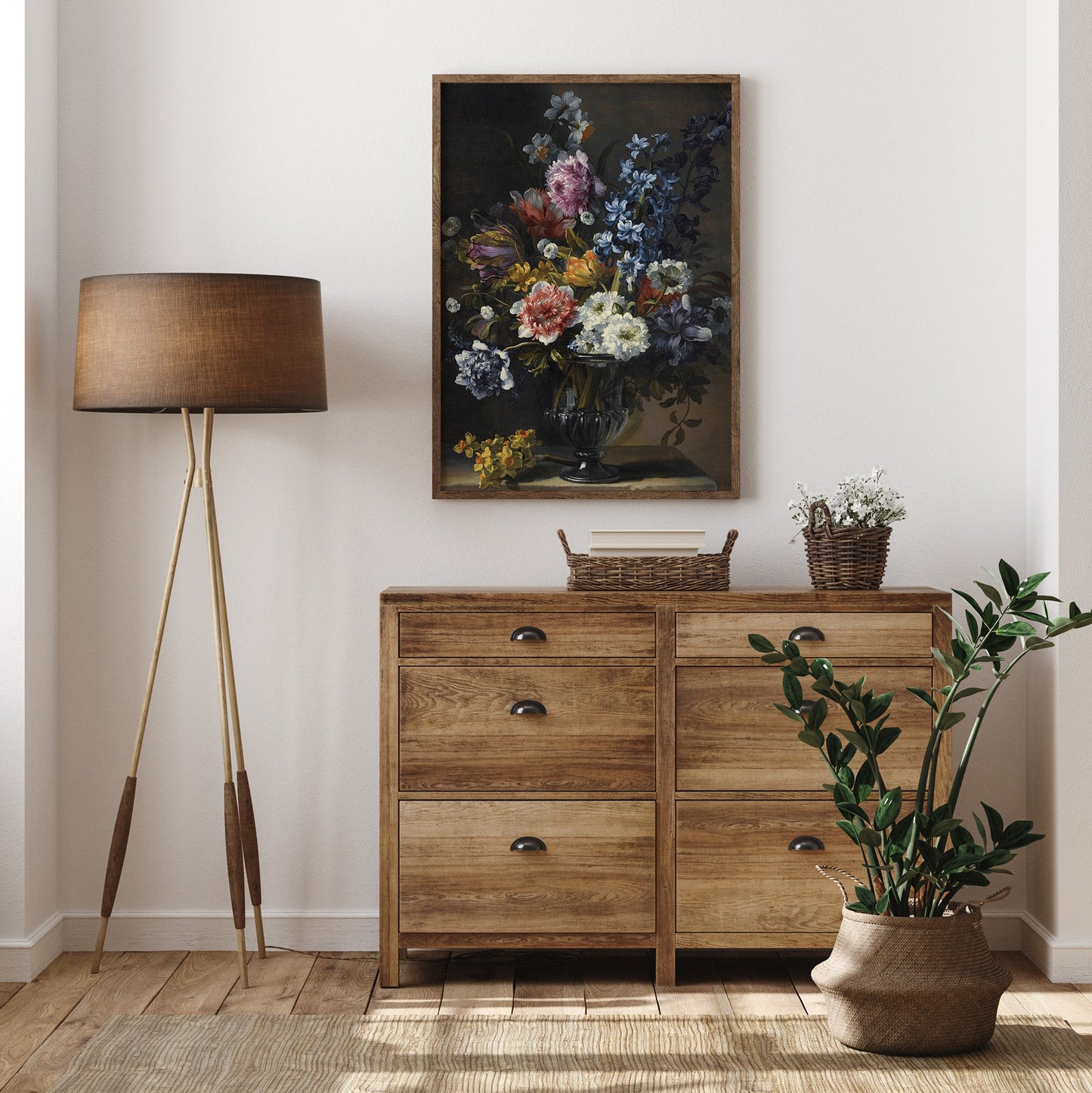 Framed floral print in a wooden frame above wooden drawers with a plant in front and next to a standard lamp.