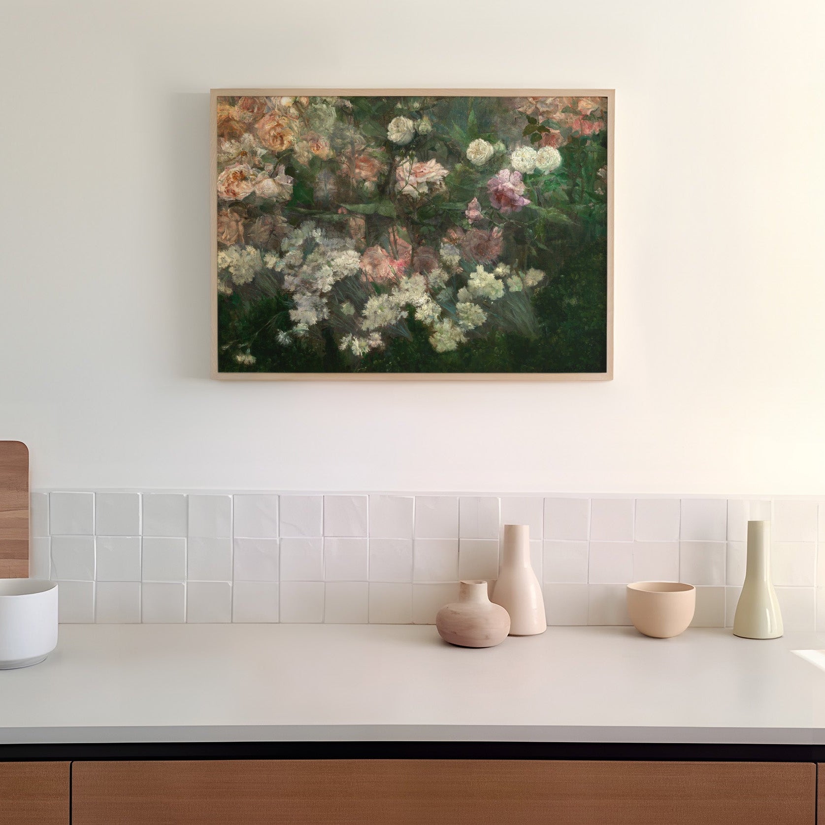 A framed art print of a rose garden in full bloom, hanging on a white wall in a kitchen above a counter top.