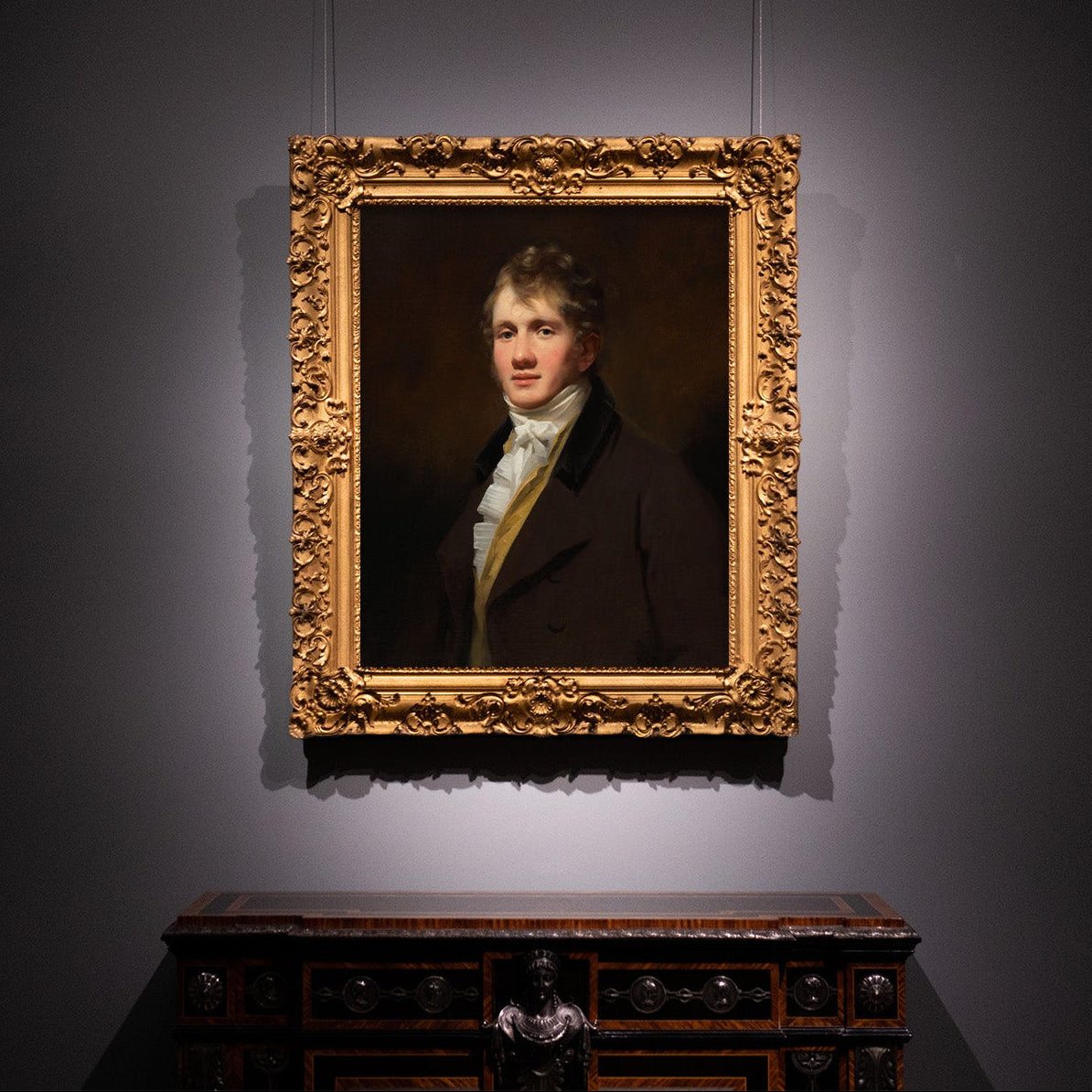 Portrait print in a gold frame on a dark wall