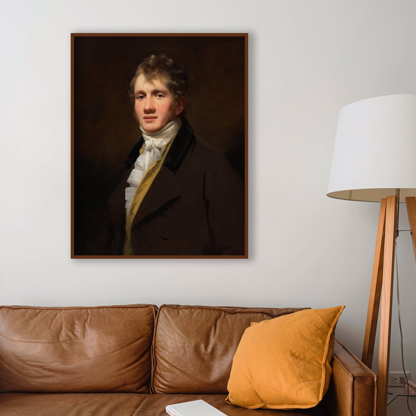 Portrait of a man in a dark coat above a brown leather sofa with a yellow pillow and a white book.