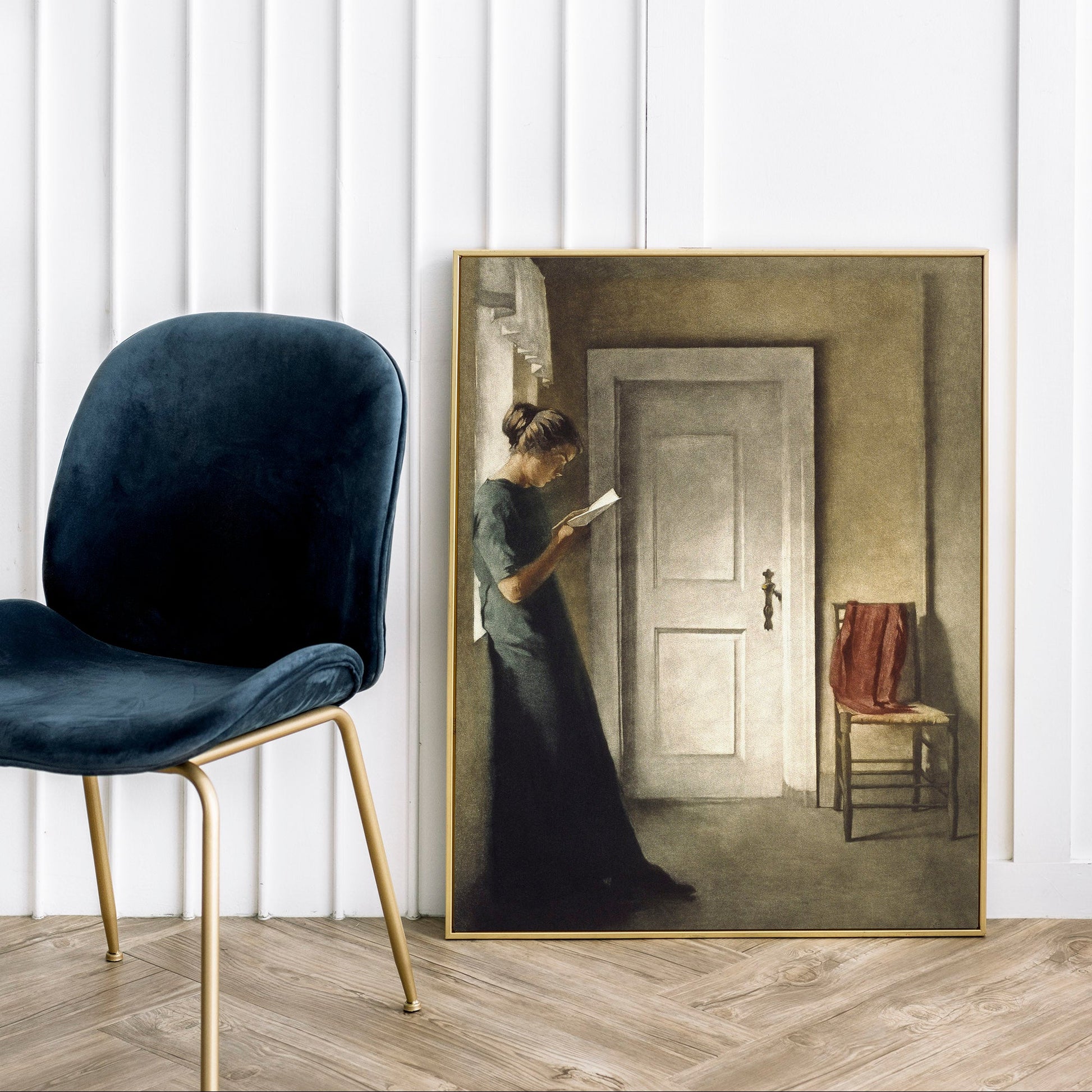 Framed painting of a woman in a room with a chair and lamp in the foreground.
