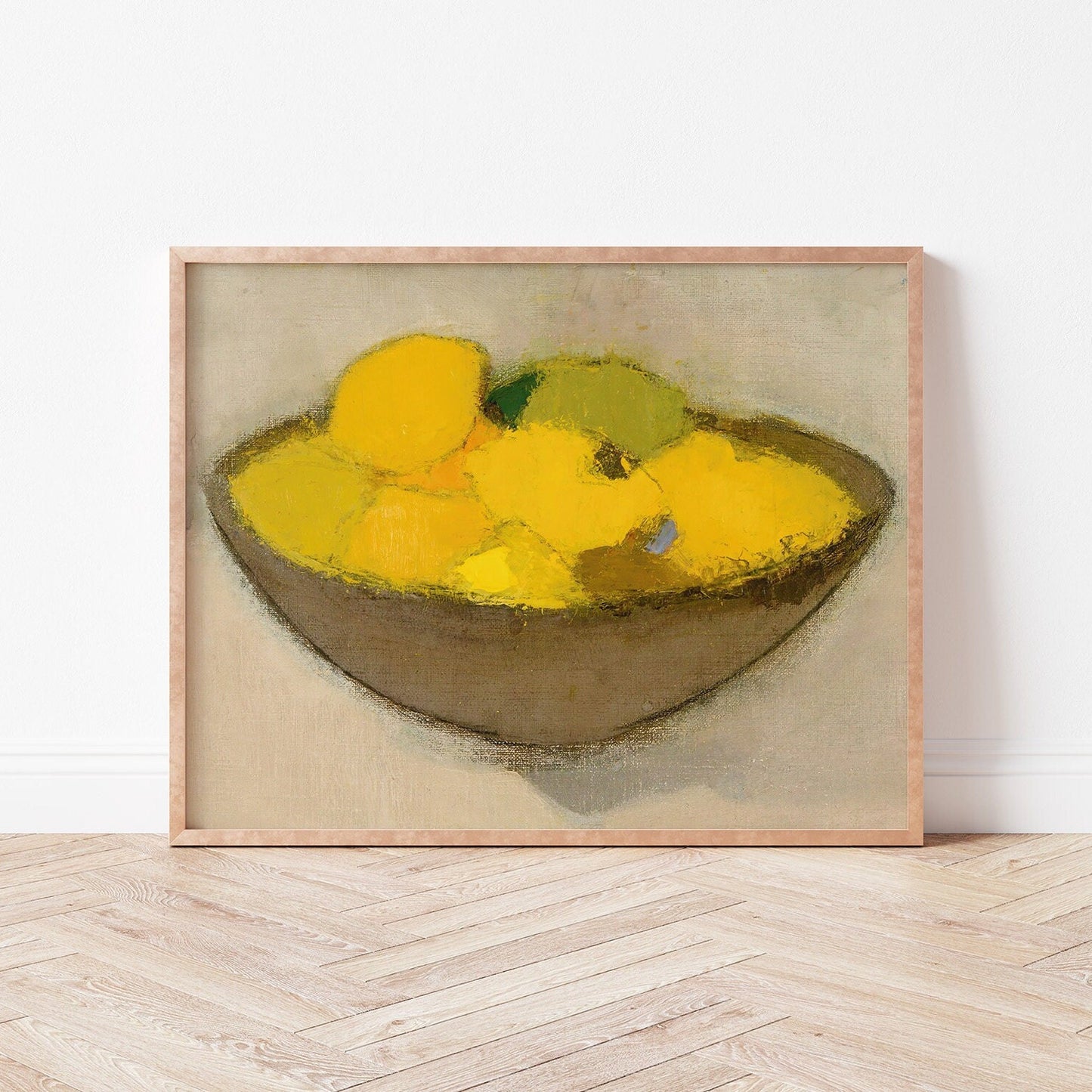 Framed print of a bowl of lemons on a neutral background, resting on a wooden floor.