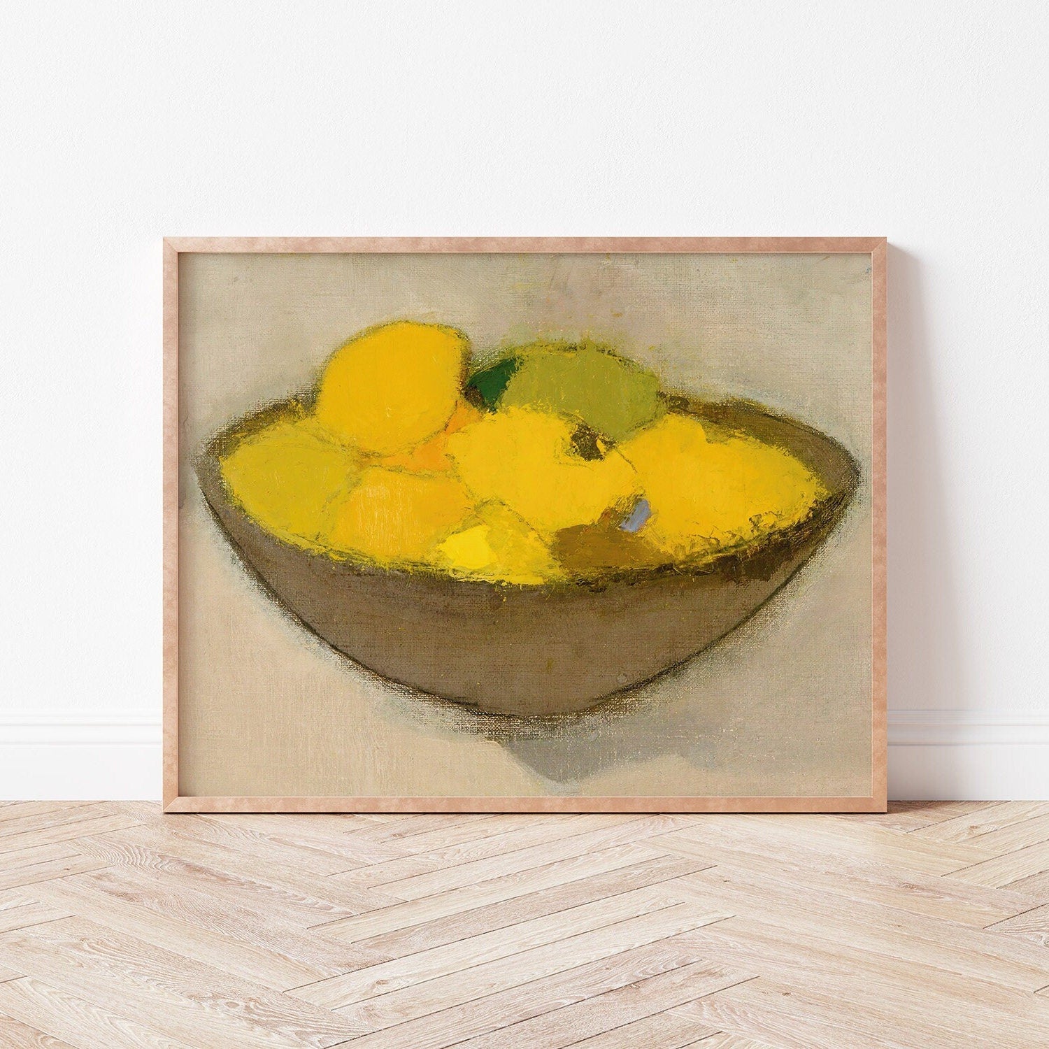 Framed print of a bowl of lemons on a neutral background, resting on a wooden floor.