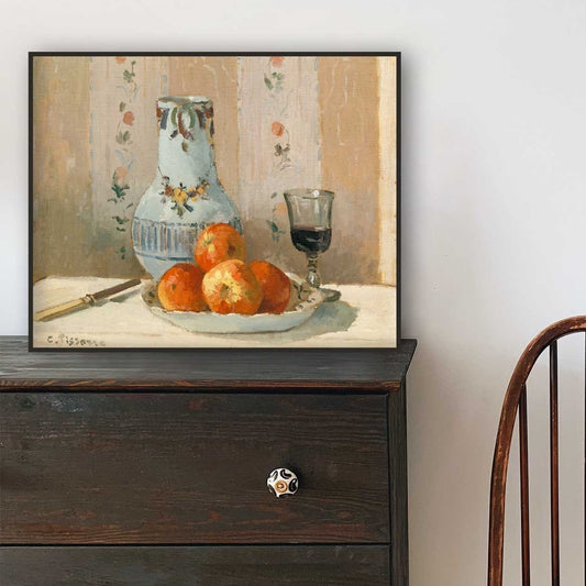 Framed still life print on a wooden dresser with a chair in the background