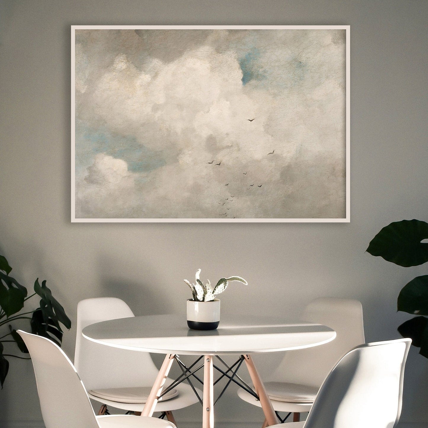 Dining area with a round table and four chairs, featuring a large cloudscape print on the wall.