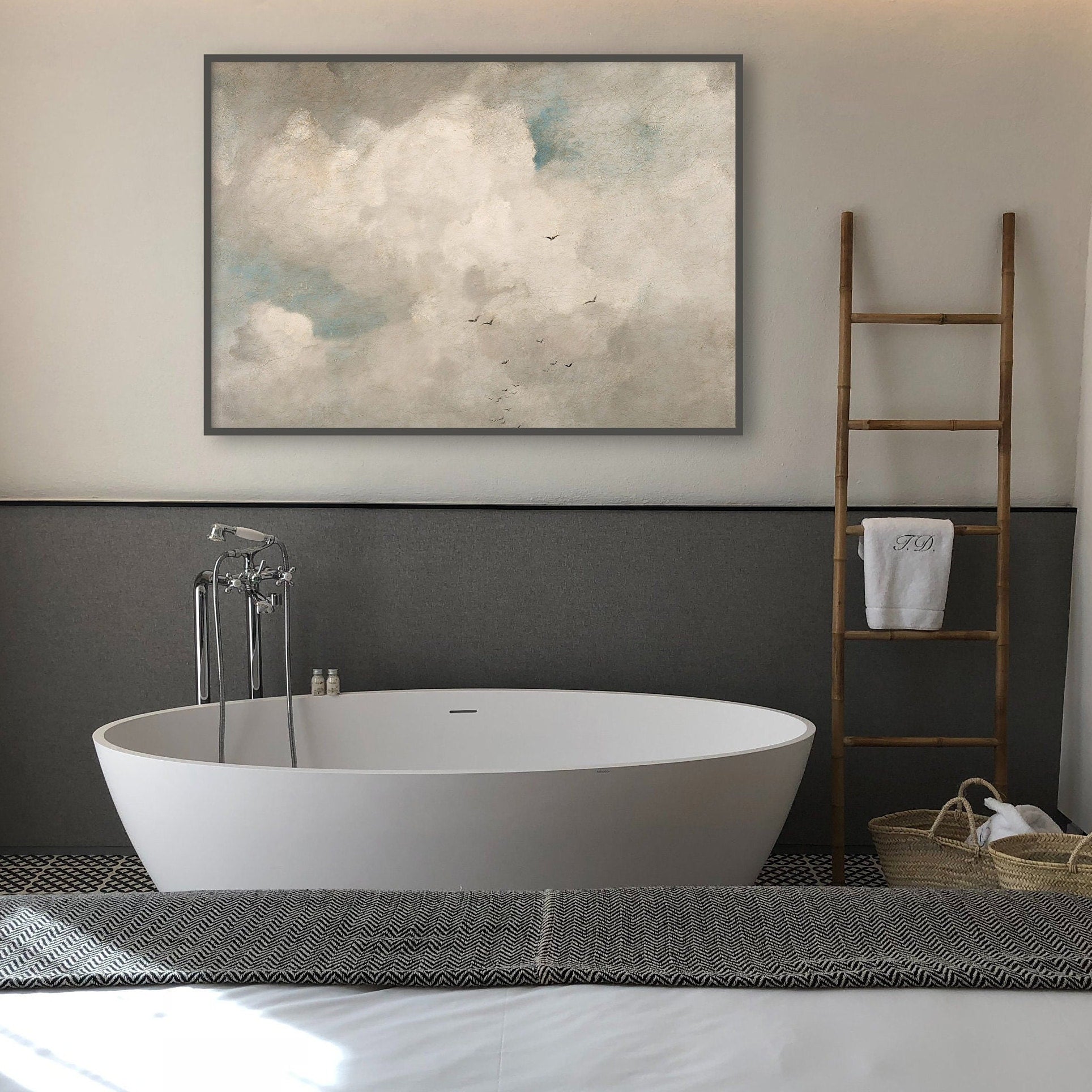 Modern bathroom with a freestanding bathtub, framed cloudscape artwork on the wall, and a wooden ladder with towels.